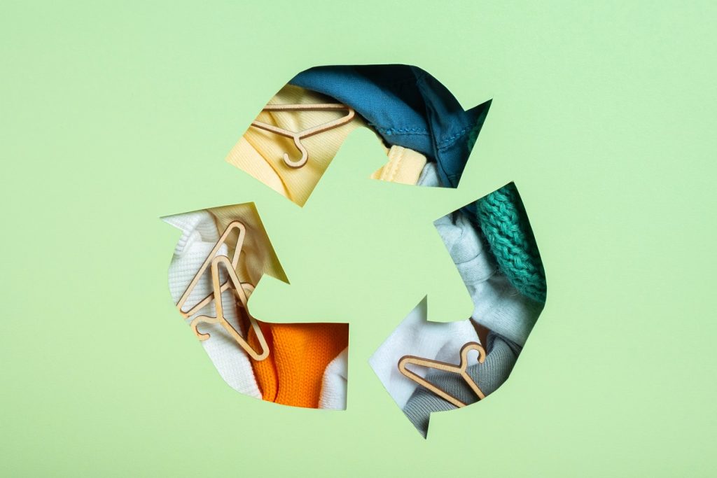 Бавната мода Paper cut recycling symbol, clothes and hangers are shown behind