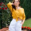 Woman dressed in yellow linen shirt with longs sleeves and coconut buttons and white pants