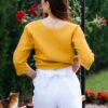 Woman dressed in yellow linen shirt with longs sleeves and coconut buttons and white pants
