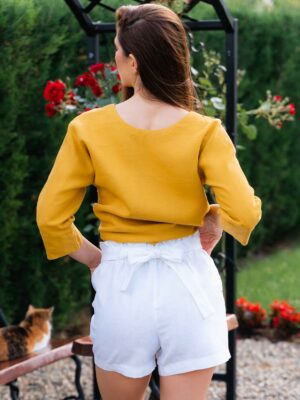 Woman dressed in yellow linen shirt with longs sleeves and coconut buttons and white pants