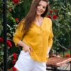 Woman dressed in yellow linen shirt with longs sleeves and coconut buttons and white pants