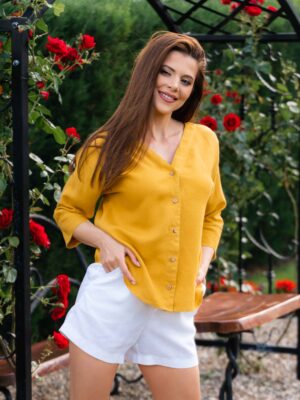 Woman dressed in yellow linen shirt with longs sleeves and coconut buttons and white pants