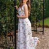 Woman wearing a long dress with colorful patterns stands in a flower garden with roses and green grass