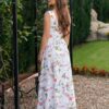 Woman wearing a long dress with colorful patterns stands in a flower garden with roses and green grass