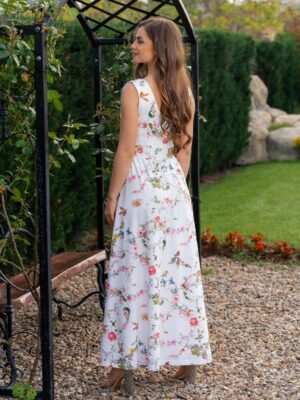 Woman wearing a long dress with colorful patterns stands in a flower garden with roses and green grass