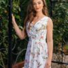 Woman wearing a long dress with colorful patterns stands in a flower garden with roses and green grass