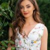 Woman wearing a long dress with colorful patterns stands in a flower garden with roses and green grass