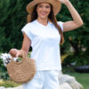 Woman wearing a white t-shirt and white long trousers with a hat on her head is holding a knitted bag