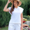 Woman wearing a white t-shirt and white long trousers with a hat on her head is holding a knitted bag