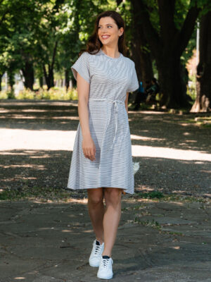 A woman wearing an organic cotton dress with a tie at the waist is walking in the park