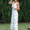Woman wearing a long dress with colorful patterns stands in a flower garden with roses and green grass