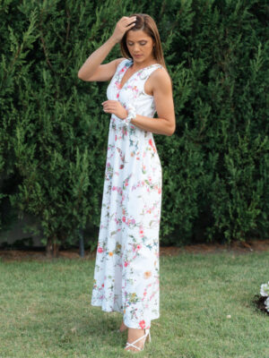Woman wearing a long dress with colorful patterns stands in a flower garden with roses and green grass