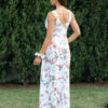 Woman wearing a long dress with colorful patterns stands in a flower garden with roses and green grass