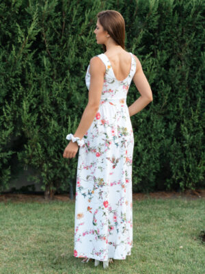 Woman wearing a long dress with colorful patterns stands in a flower garden with roses and green grass