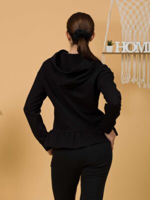 Woman with brown hair wearing black long-sleeved sweatshirt with a hood and ruffles, and black organic cotton long pants