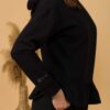 Woman with brown hair wearing black long-sleeved sweatshirt with a hood and ruffles, and black organic cotton long pants