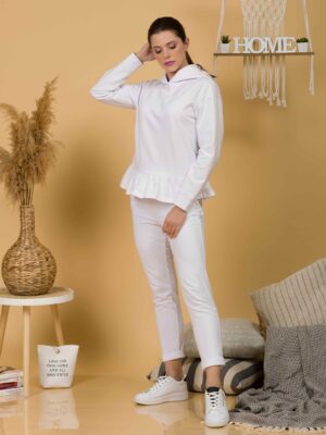 Woman with brown hair wearing white long-sleeved sweatshirt with a hood and ruffles and white organic cotton long pants