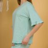 Woman with blond hair wearing turquoise organic cotton pajama set of short sleeve blouse and long pants