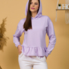 Woman with brown hair wearing violet long-sleeved sweatshirt with a hood and ruffles, and white organic cotton long pants