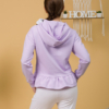Woman with brown hair wearing violet long-sleeved sweatshirt with a hood and ruffles, and white organic cotton long pants