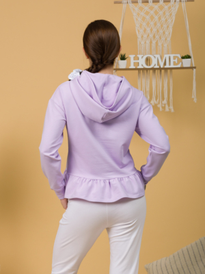 Woman with brown hair wearing violet long-sleeved sweatshirt with a hood and ruffles, and white organic cotton long pants