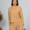 Woman with blond hair wearing organic cotton caramel color blouse with semi-polo neck and white caramel color long pants