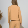 Woman with blond hair wearing organic cotton caramel color blouse with semi-polo neck and white caramel color long pants