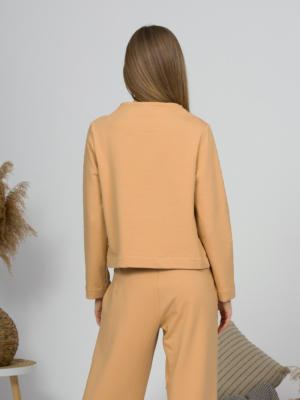 Woman with blond hair wearing organic cotton caramel color blouse with semi-polo neck and white caramel color long pants