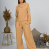 Woman with blond hair wearing organic cotton caramel color blouse with semi-polo neck and white caramel color long pants