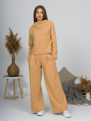Woman with blond hair wearing organic cotton caramel color blouse with semi-polo neck and white caramel color long pants
