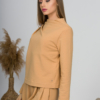 Woman with blond hair wearing organic cotton caramel color blouse with semi-polo neck and white caramel color long pants