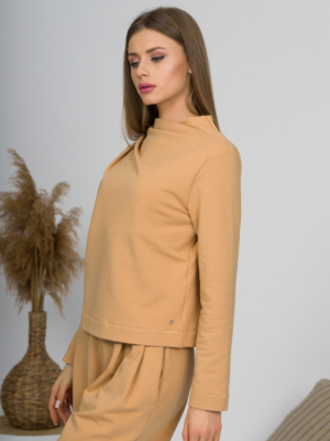 Woman with blond hair wearing organic cotton caramel color blouse with semi-polo neck and white caramel color long pants