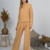Woman with blond hair wearing organic cotton caramel color blouse with semi-polo neck and white caramel color long pants