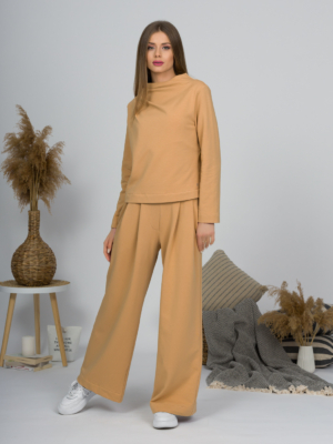 Woman with blond hair wearing organic cotton caramel color blouse with semi-polo neck and white caramel color long pants