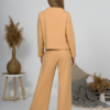 Woman with blond hair wearing organic cotton caramel color blouse with semi-polo neck and white caramel color long pants