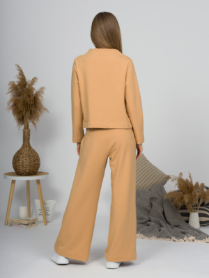 Woman with blond hair wearing organic cotton caramel color blouse with semi-polo neck and white caramel color long pants