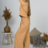 Woman with blond hair wearing organic cotton caramel color blouse with semi-polo neck and white caramel color long pants