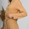 Woman with blond hair wearing organic cotton caramel color blouse with semi-polo neck and white caramel color long pants