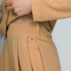 Woman with blond hair wearing organic cotton caramel color blouse with semi-polo neck and white caramel color long pants