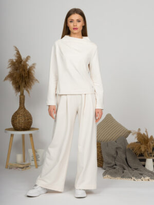 Woman with blond hair wearing organic cotton white blouse with semi-polo neck and white wide long pants