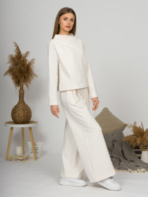 Woman with blond hair wearing organic cotton white blouse with semi-polo neck and white wide long pants