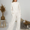 Woman with blond hair wearing organic cotton white blouse with semi-polo neck and white wide long pants