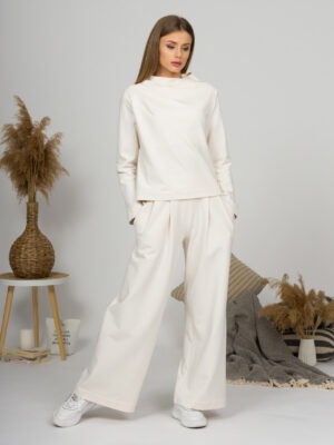 Woman with blond hair wearing organic cotton white blouse with semi-polo neck and white wide long pants