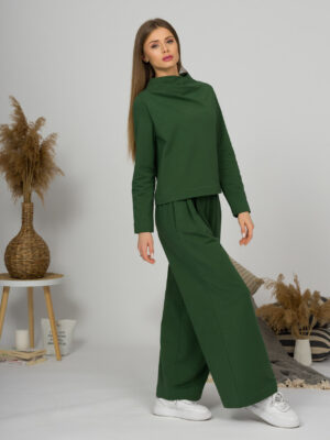 Woman with blond hair wearing organic cotton dark green color blouse with semi-polo neck and white dark green color long pants