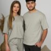 A young woman with blond hair wearing organic cotton gray t-shirt and gray straight leg trousers and a young man with black hair wearing organic cotton gray t-shirt and black trousers