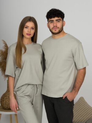 A young woman with blond hair wearing organic cotton gray t-shirt and gray straight leg trousers and a young man with black hair wearing organic cotton gray t-shirt and black trousers
