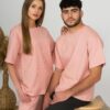 A young woman with blond hair wearing organic cotton pink t-shirt and pink straight leg trousers and a young man with black hair wearing organic cotton pink t-shirt and black trousers
