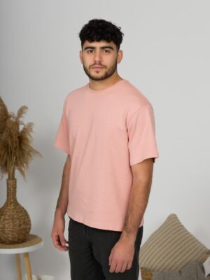 a young man with black hair wearing organic cotton pink t-shirt and black trousers