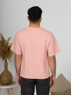 a young man with black hair wearing organic cotton pink t-shirt and black trousers