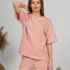 A young woman with blond hair wearing organic cotton pink t-shirt and pink straight leg trousers